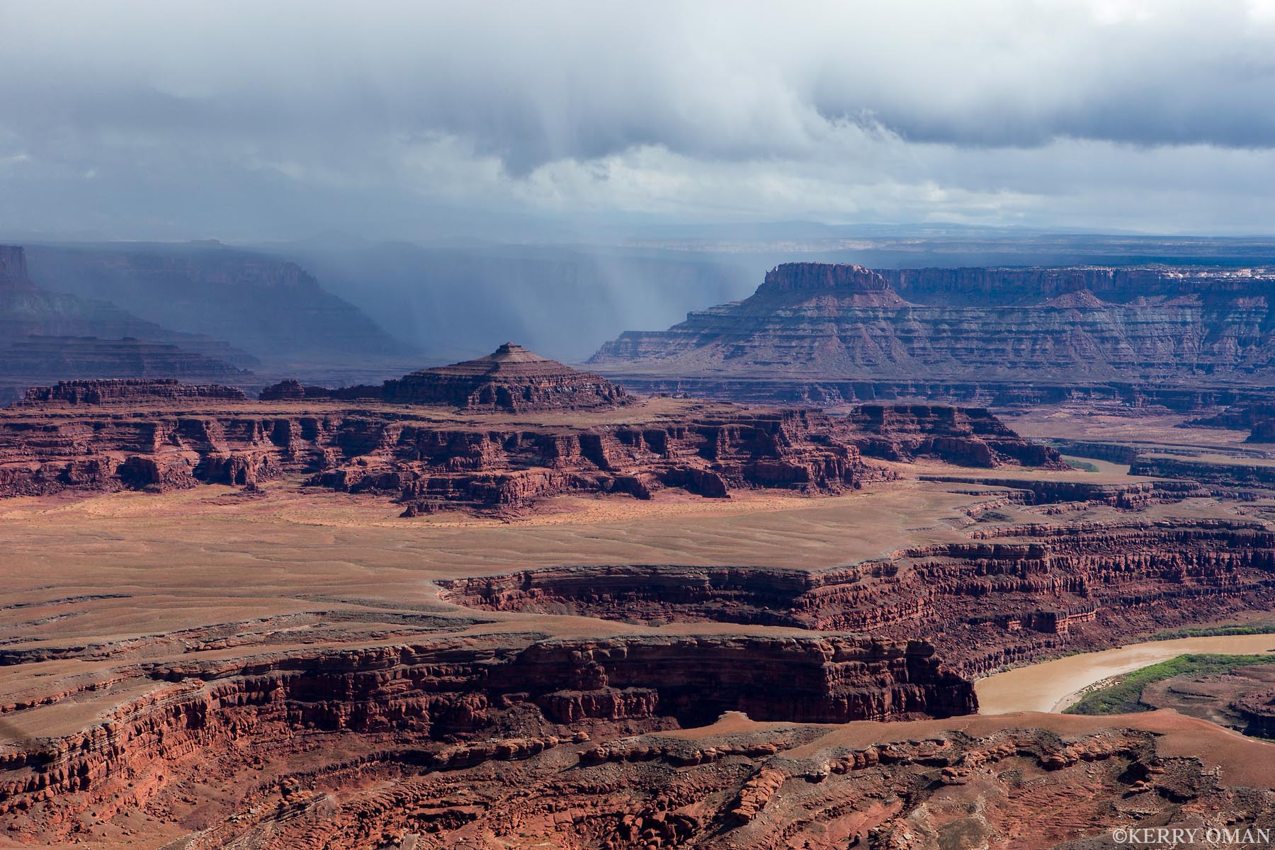 Storm Over the Canyonlands From Dead Horse Point, a storm drifts across the canyon country, casting shadows over the layered red rock mesas and buttes of...