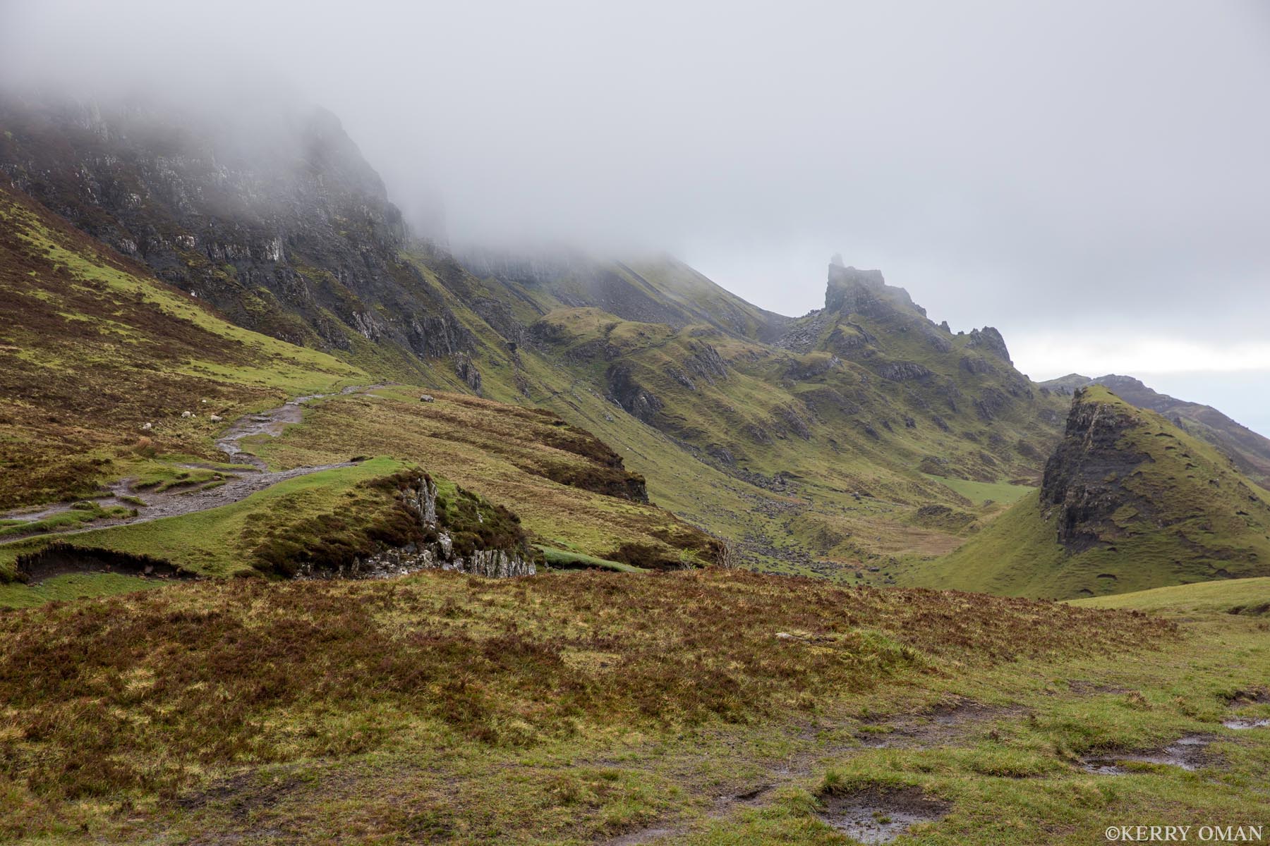 Into the Fold Cloud drapes the ridgelines of the Quiraing as a footpath winds through ancient Highland terrain. Jagged rock formations rise...