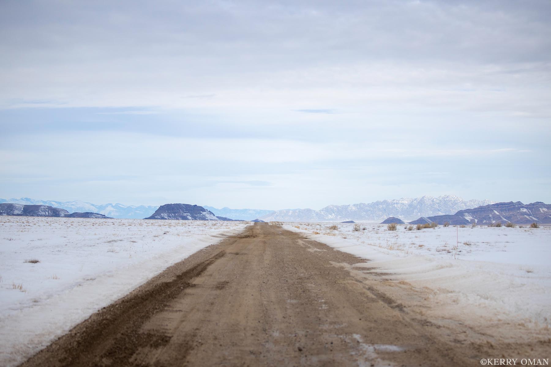 Winter Passage A dirt road stretches across the snow-covered floor of Utah’s west desert, leading toward distant mesas and a wall of mountains...